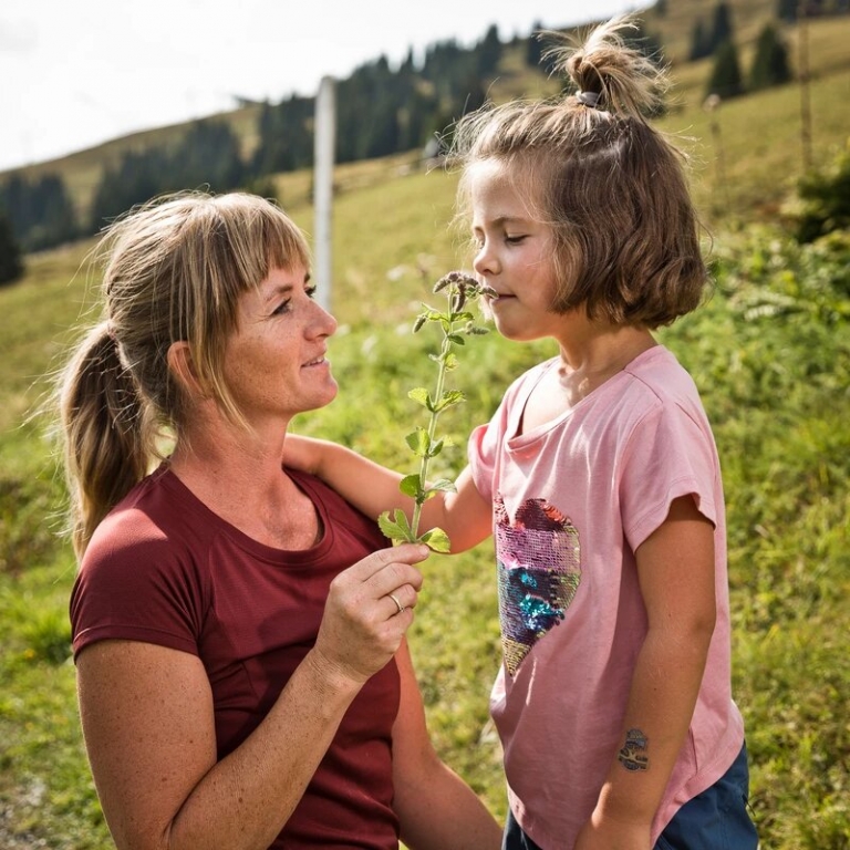 Mama mit Mädchen auf Wiese hält ihrer Tochter Blumen zum Riechen hin
