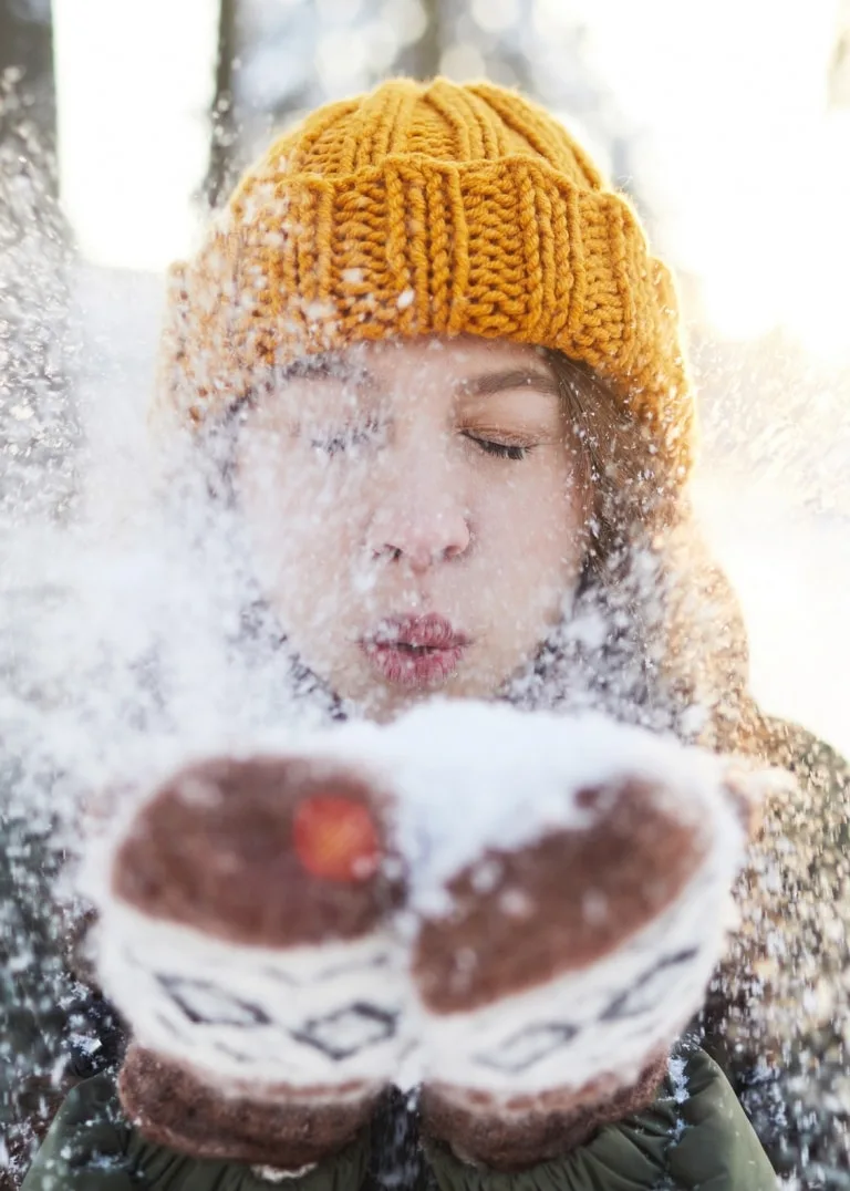 Winterfreuden Frau mit oranger Mütze pustet Schnee in Kamera