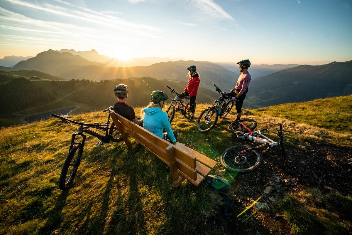 4 Mountainbiker ruhen sich auf Bank aus und bewundern Sonnenuntergang