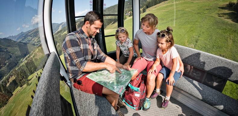 Familie in Sommerbahn-Gondel schaut auf Karte