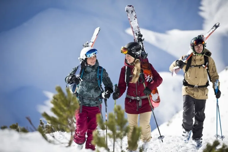 Sonnenski 3er Gruppe geht beschneiten Hang hinauf mit Skiern auf den Schultern
