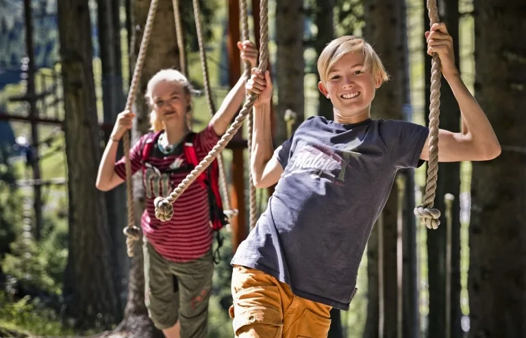 Baumzipfelweg und Golden Gate Bridge der Alpen 2 Kinder im Klettergarten halten sich an Seilen
