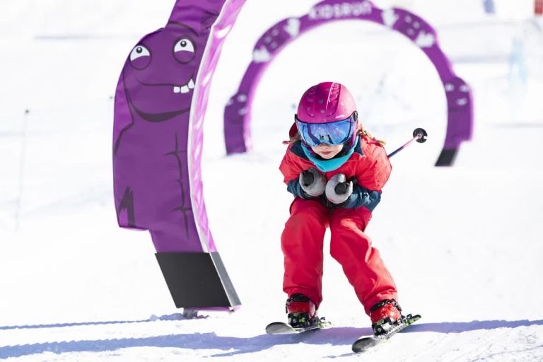Mädchen in rotem Skianzug fährt Schneepflug