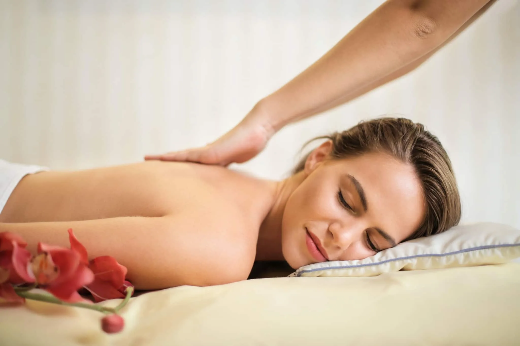Wellness Massage Frau liegt mit geschlossenen Augen auf Bank und bekommt Rückenmassage