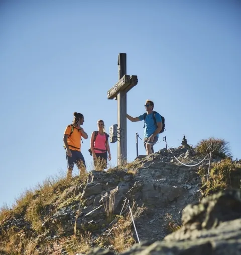 Wandern in Saalbach Hinterglemm 3 Wanderer stehen bei Gipfelkreuz