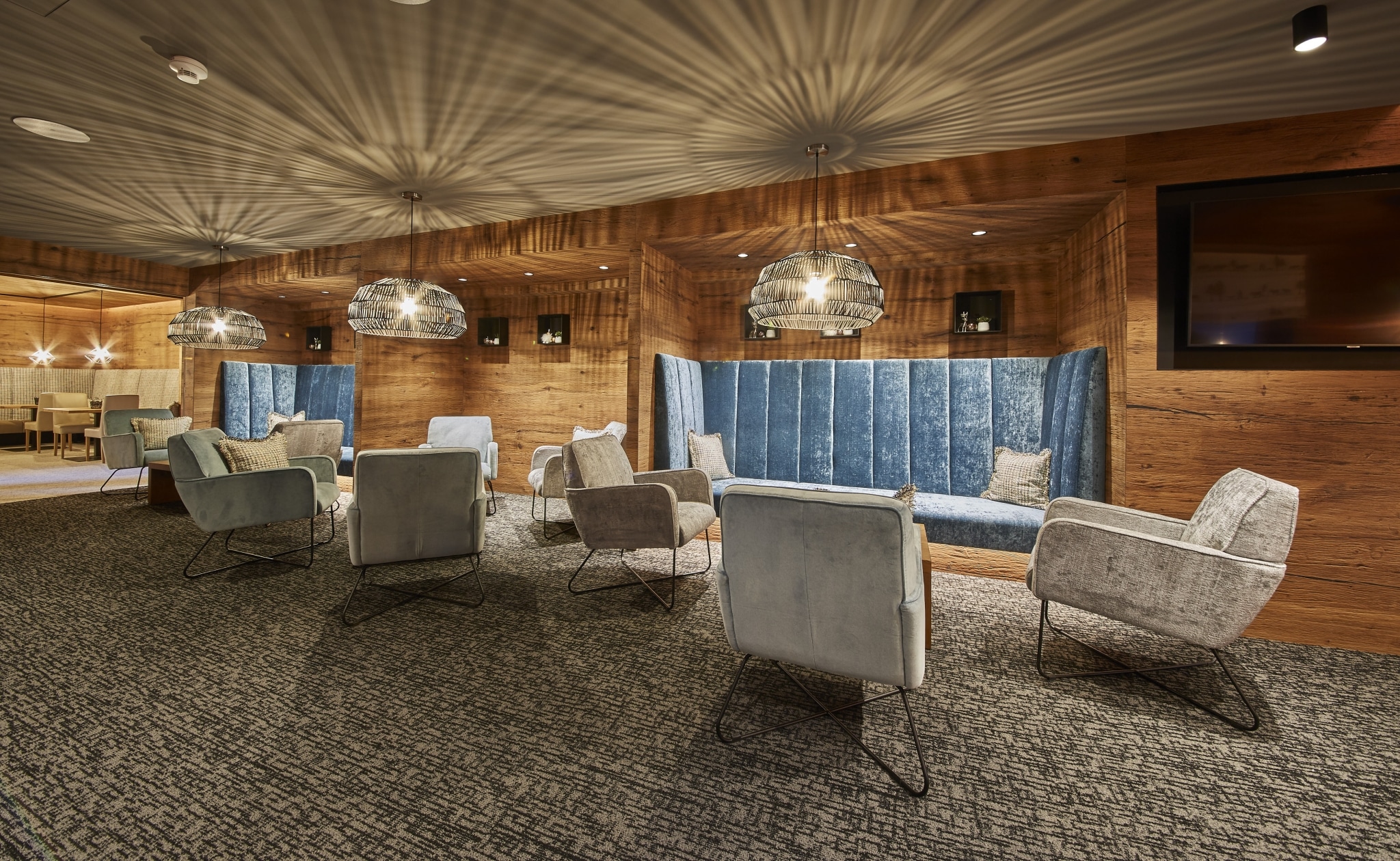 Die Lounge mit modernen Hängelampen, gemütlichen grauen Sesseln und blauen Eckbänken
