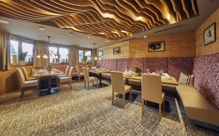 Speisesaal mit roter Eckbank Speisesaal mit einem Design-Holzelement und vier gedeckten Tischen.