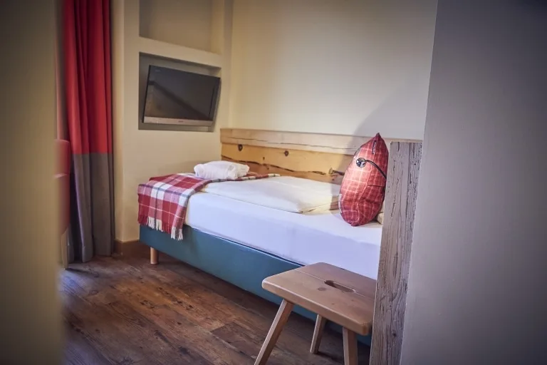 Einzelbett im Einzelzimmer Ein Einzelbett mit weißer Bettdecke und rotem Polster sowie einem TV über dem Bettende