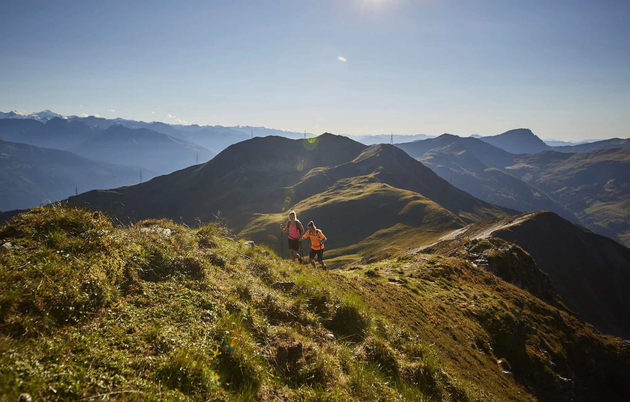 Wandern in Saalbach Hinterglemm Zwei Wanderer gehen über eine Almwiesen-Kuppe bergaufwärts, im Hintergrund die Salzburger Berwelt