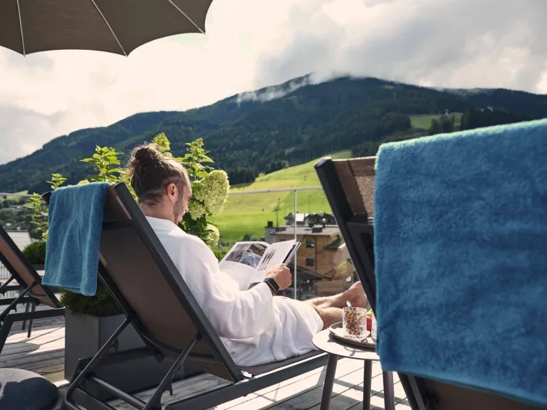 Entspannen auf dem Rooftop Ein Mann liest eine Zeitschrift und liegt auf dem Liegestuhl auf der Dachterrasse