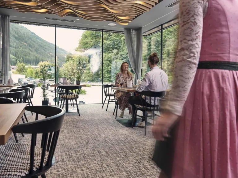 Restaurantbereich im Hotel Hasenauer Eine Restaurantkraft geht in den Speisesaal, zwei Personen sitzen am Tisch
