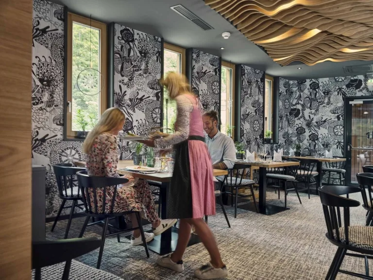 Restaurant-Service im Hotel Hasenauer Eine Restaurantkraft serviert das Essen zu eine Tisch mit zwei Personen