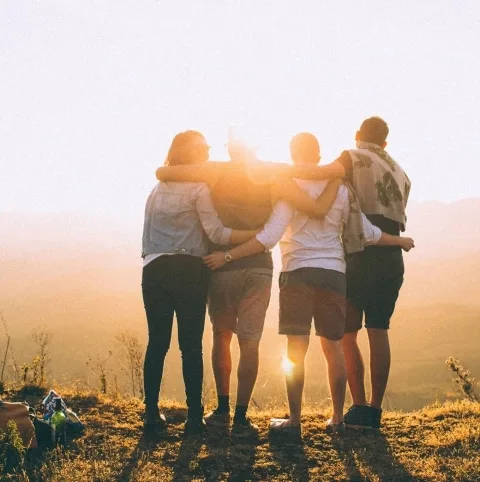 Teamspirit Vier Menschen stehen auf einer Wiese und haben die Sonne im Hintergrund