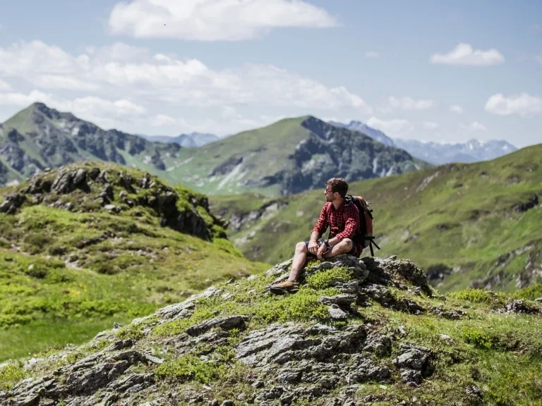 Mann in der Bergwiese EIn Mann sitzt auf einer grünen Wiese mitten in den Bergen