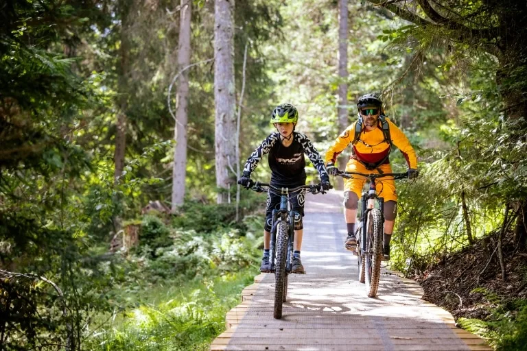 Trail Action für Groß und Klein 2 Personen fahren auf einem Holzsteg mit dem Bike