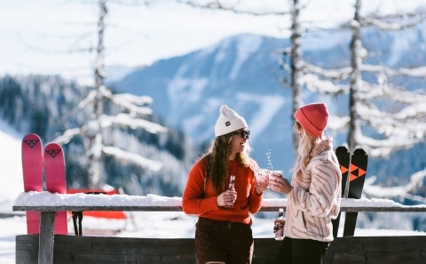 Gemeinsame Zeit beim Skifahren in Saalbach Hinterglemm Zwei Frauen stehen am Geländer und trinken etwas