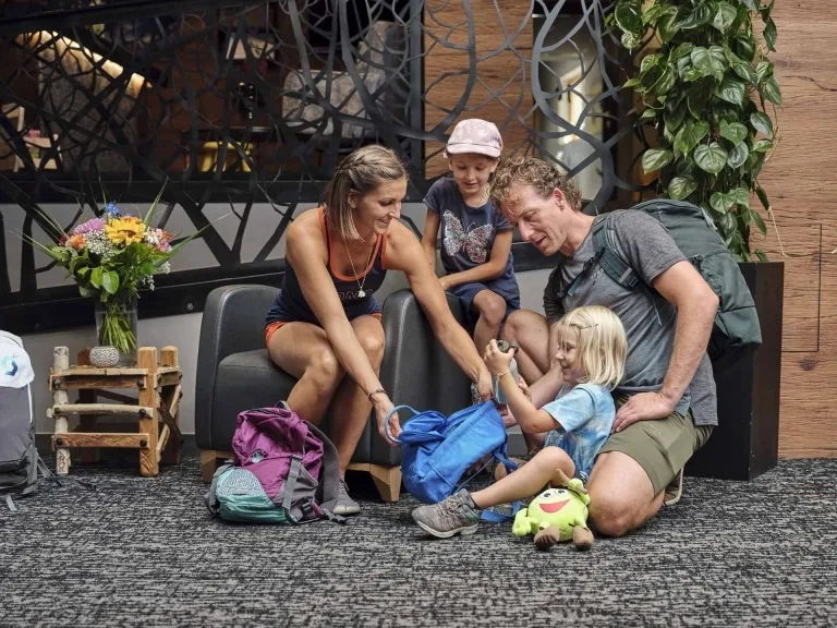 Rucksack für die Familienwanderung Kind hält Trinkflasche in der Hand, sitzt am Boden in der Lobby und packt den Rucksack mit der Familie.