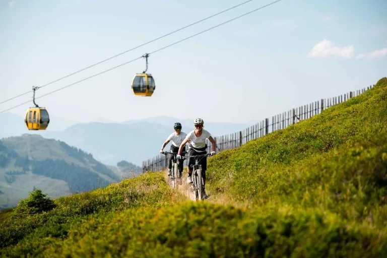 Bike Sommer 2022 (1) Zwei Frauen fahren über eine Bikestrecke am Berg. Im Hintergrund sieht man die Gondel
