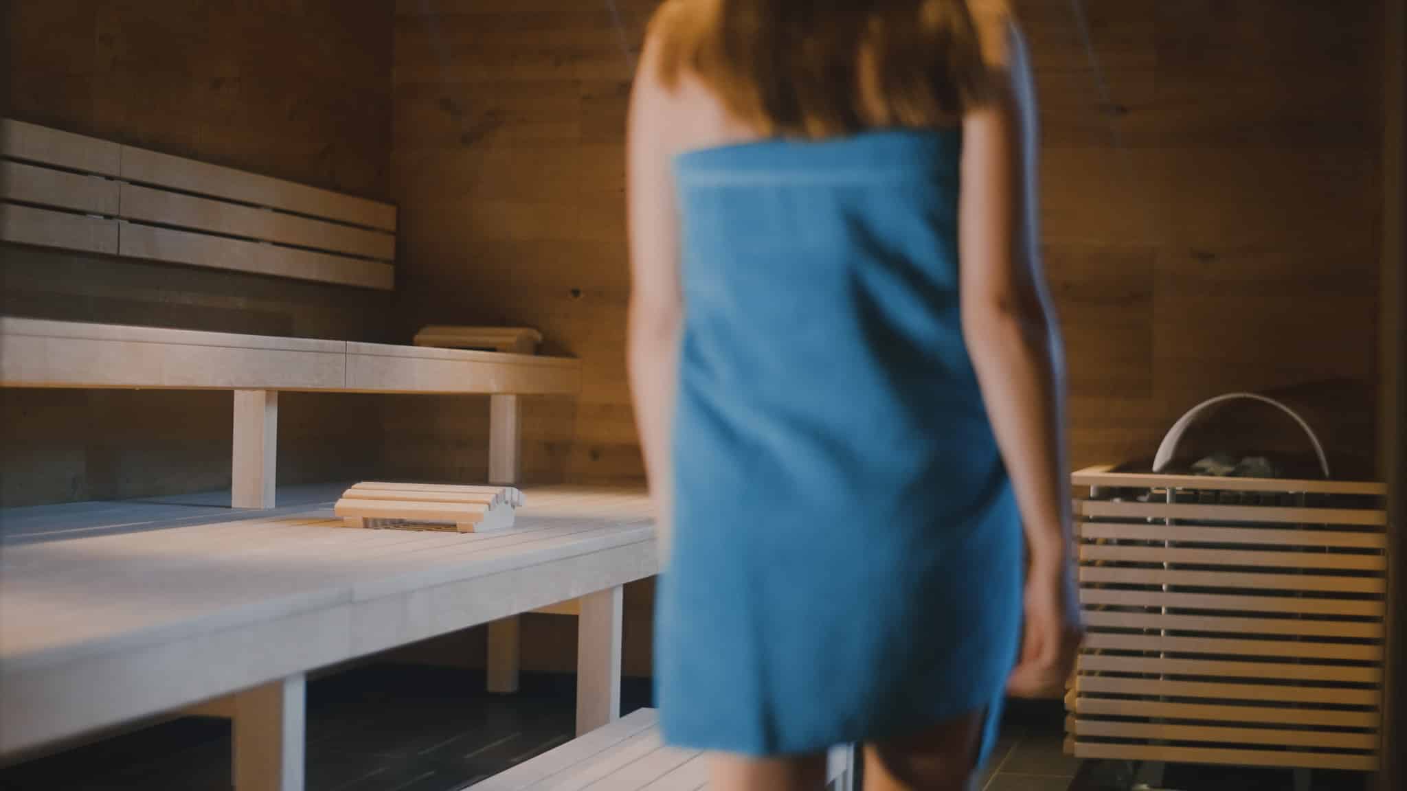 Frau geht in der Sauna zum Saunaofen