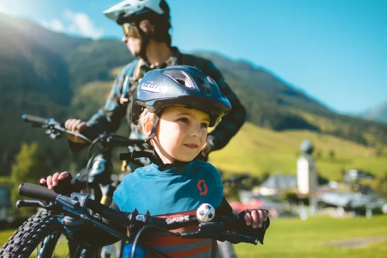 © saalbach.com, Mia Knoll (2) Kind im Bikecircus. Im Hintergrund steht ein Mann und blickt in die Ferne. Noch weiter im Hintergrund ist eine grüne Landschaft zu sehen