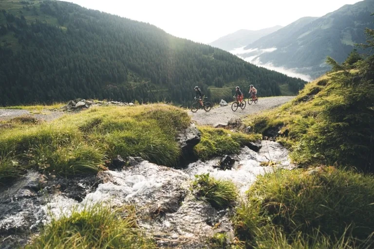 Mountainbiking in Saalbach Hinterglemm-c-saalbach.com, Moritz Ablinger 3 Biker auf Bikestrecke, die sich neben einem Gebirgsbach entlang zieht