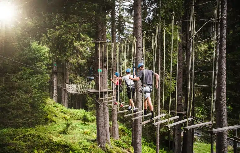 Hochseilpark _ High Rope Course © saalbach.com Besucher des Hochseilparks in Saalbach Hinterglemm klettern über ein gesichertes Seilparcours-Element zwischen hohen Bäumen